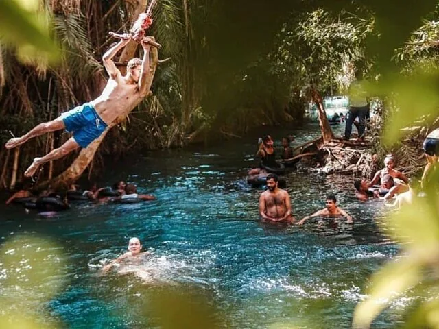 Menschen, die schwimmen und sich an einem Seil in die Chemka Hot Springs schwingen.