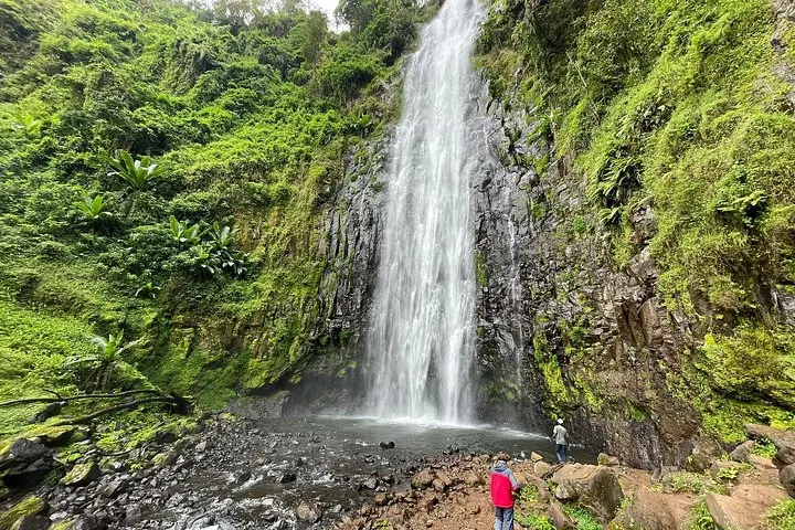 Zwei Personen stehen neben einem hohen Wasserfall, der eine felsige Klippe hinabstürzt.