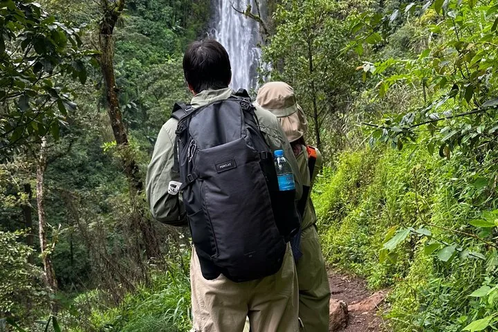 Zwei Wanderer mit Rucksäcken gehen auf einem Pfad in Richtung eines Wasserfalls.